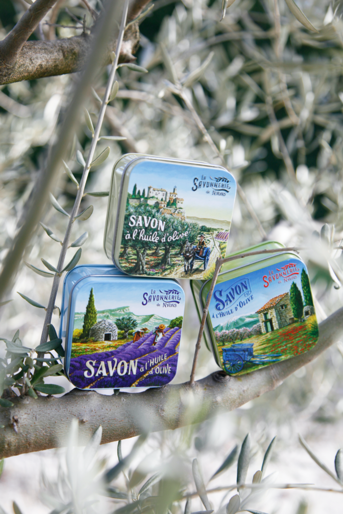 Mise en scene de 3 boites à savon vintage en metal illustré par des paysages provençaux posés sur une branche d'olivier - Fabriqué en France par La Savonnerie de Nyons