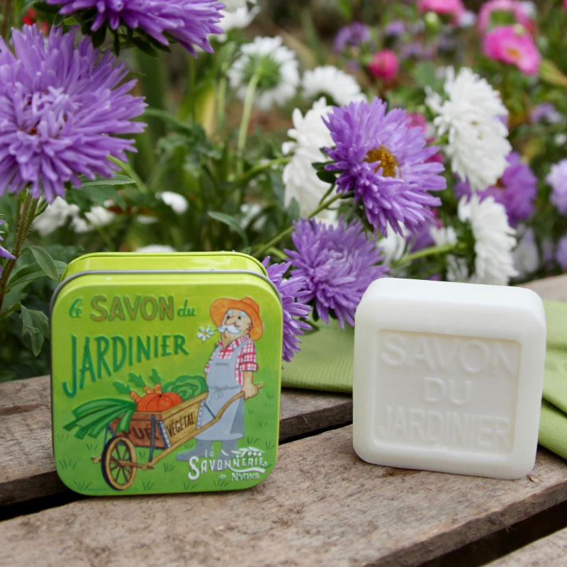 Savon du jardinier de 100 g dans sa jolie boite en metal verte à l'esprit vintage posée dans un jardin en fleur - Fabrication traditionnelle française par La Savonnerie de Nyons