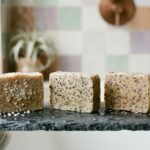 Trois savons exfoliants à grains, sel, noyaux d'olive et son de blé, sur une ardoise mouillée avec un loofah - illustration, La Savonnerie de Nyons