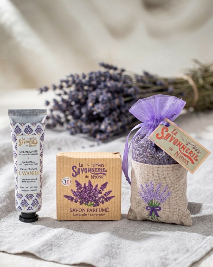 Crème mains, savon parfumé et sachet de lavande de La Savonnerie de Nyons devant un bouquet de lavande, format portrait - La Savonnerie de Nyons